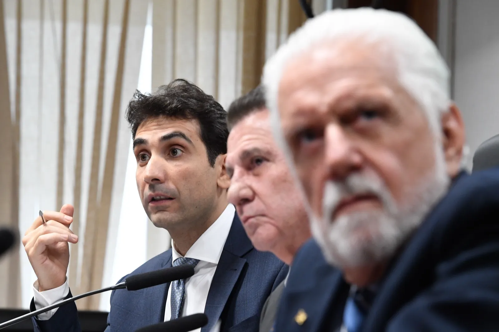 Gabriel Galípolo fala ao microfone durante sabatina no Senado, com dois senadores ao lado