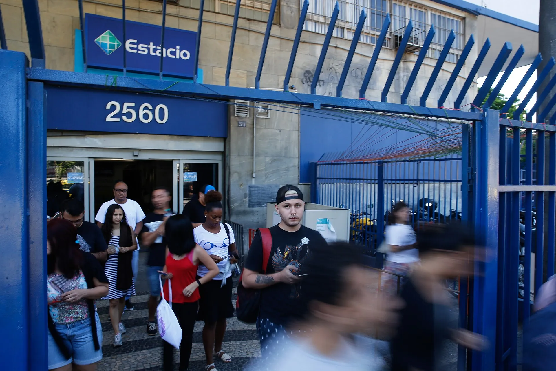 Candidatos saem de um local de prova do Enem, a Universidade Estácio de Sá, no Rio de Janeiro, por um portão azul.