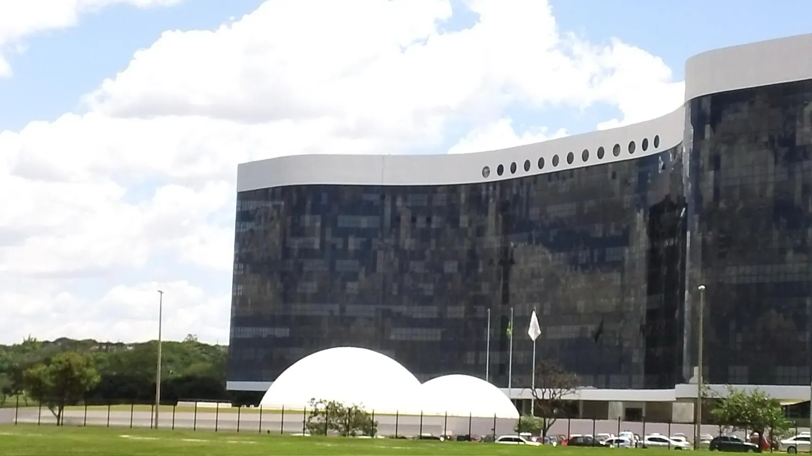 Prédio curvo de fachada espelhada escura do Tribunal Superior Eleitoral, com duas cúpulas brancas e bandeiras em frente